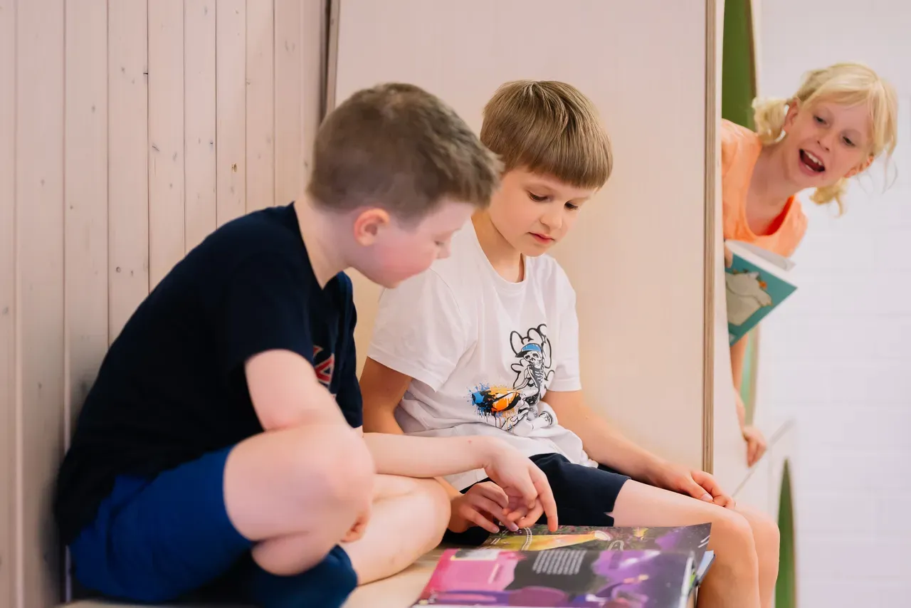 Drei Kinder in einer Kita, zwei brünette Jungen, ein blondes Mädchen, die ein Buch lesen
