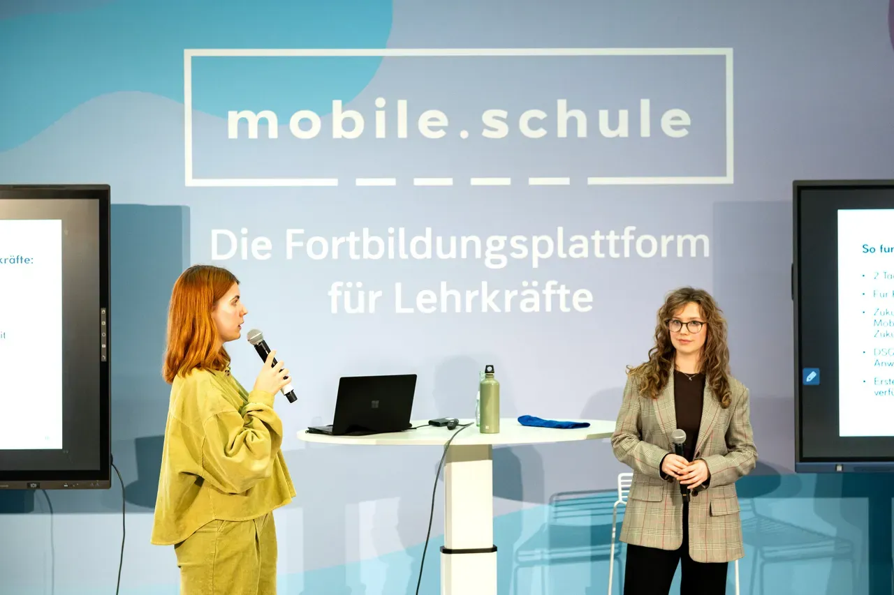Zwei Frauen halten einen Vortrag auf einer Bühne. Mit dem Schriftzug mobile.schule: Die Fortbildungsplattform für Lehrkräfte.